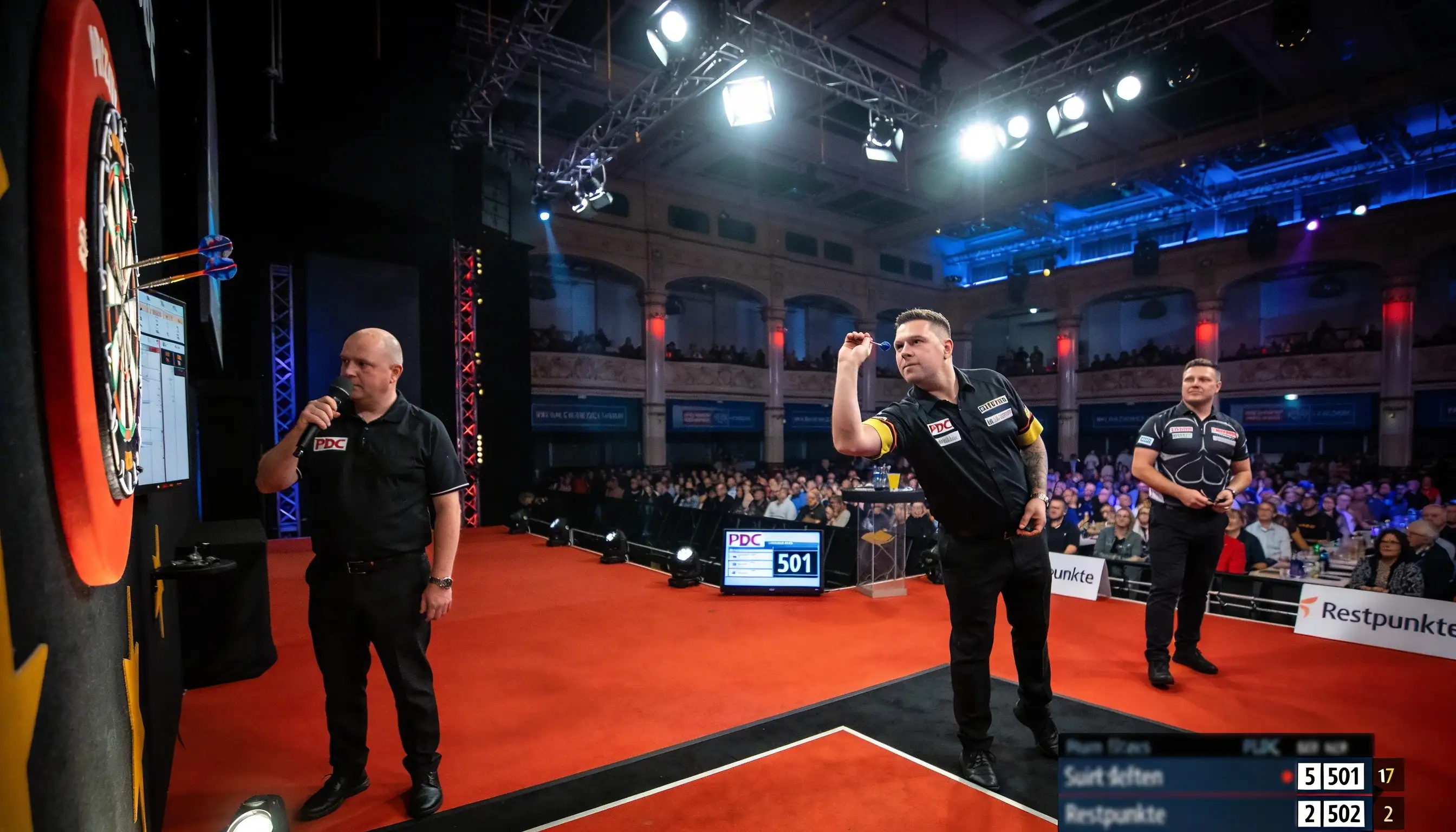 Professioneller Darts-Spieler wirft auf beleuchtetes Board vor Publikum in einer Arena